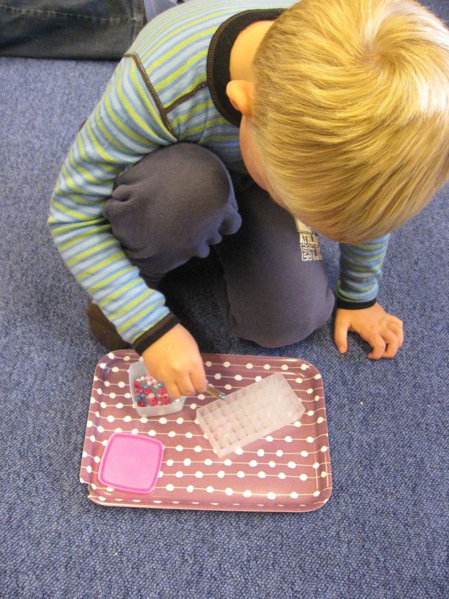 Perler legges i beholder med hjelp av pinsett.